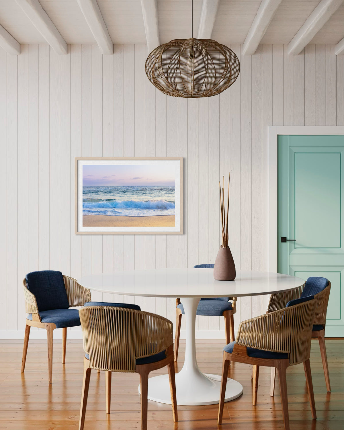 White round table with five wicker chairs, Ocean Waves artwork, mint door in a bright Laguna Beach room.