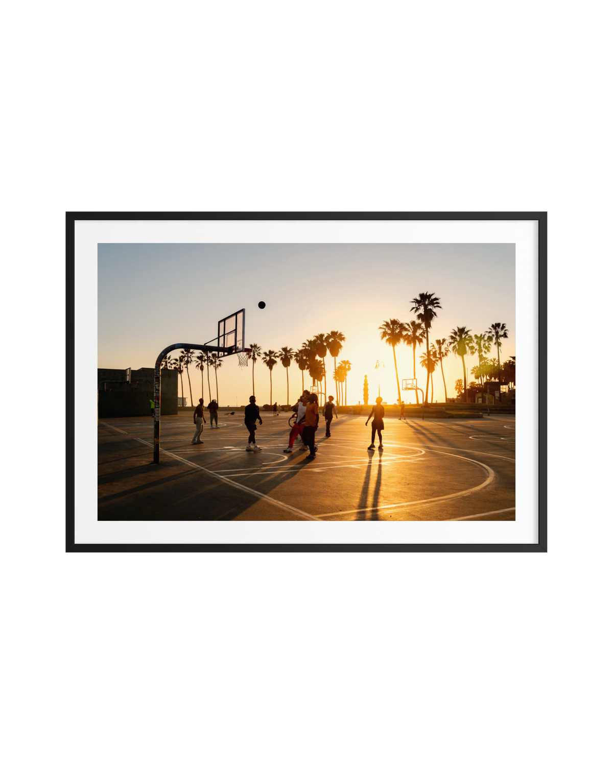 Basketball game at sunset on Venice Beach, Los Angeles, with palm trees silhouetted behind the outdoor court.