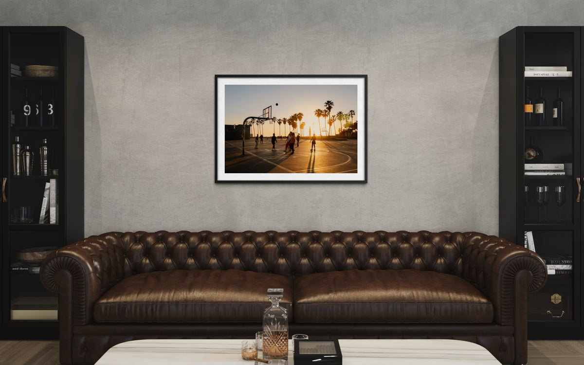 Framed “One More Game” print displayed above a brown leather sofa in a modern living room setting.