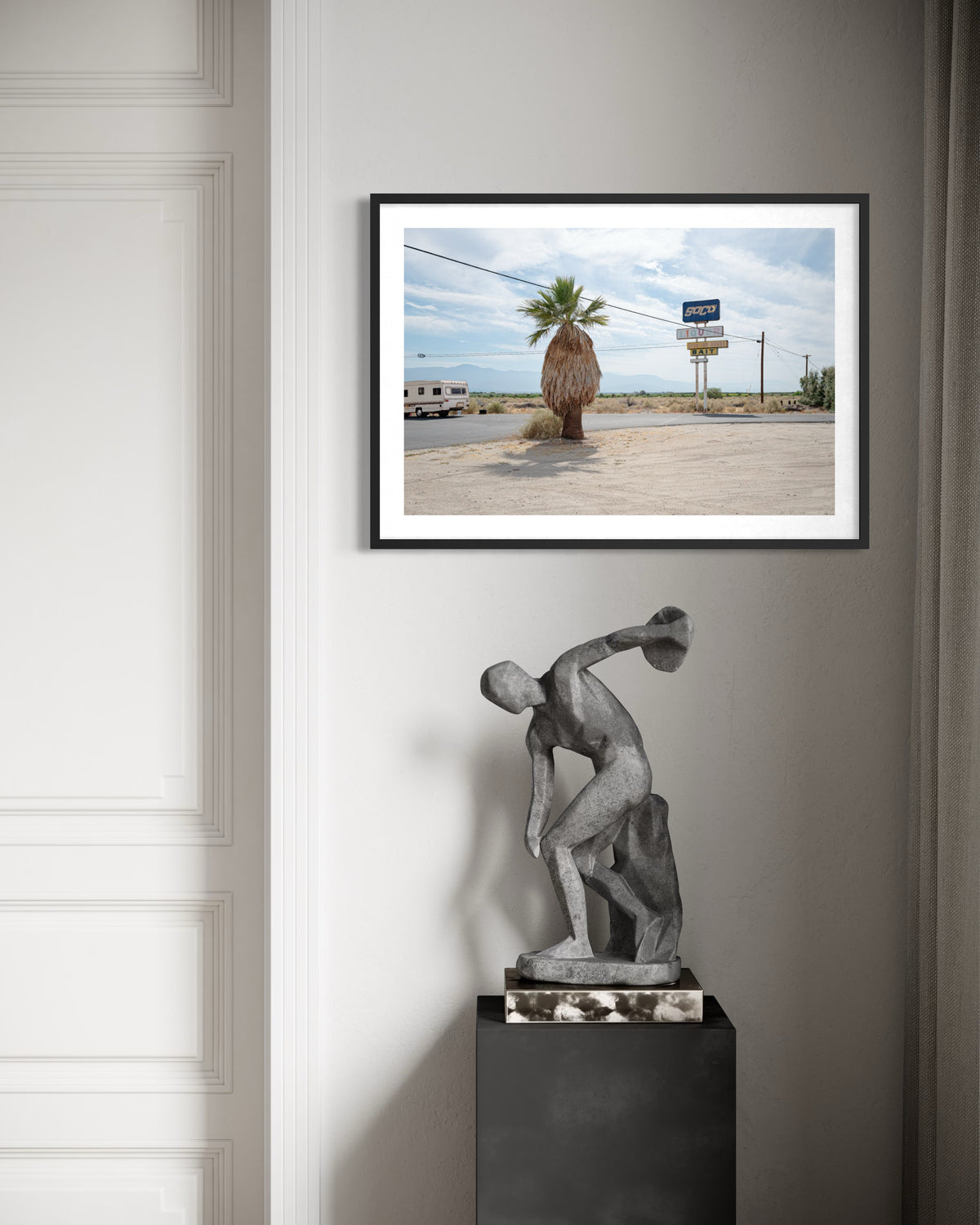 Framed Palm Desert roadside landscape displayed above a modern stone sculpture in a minimalist room setting.