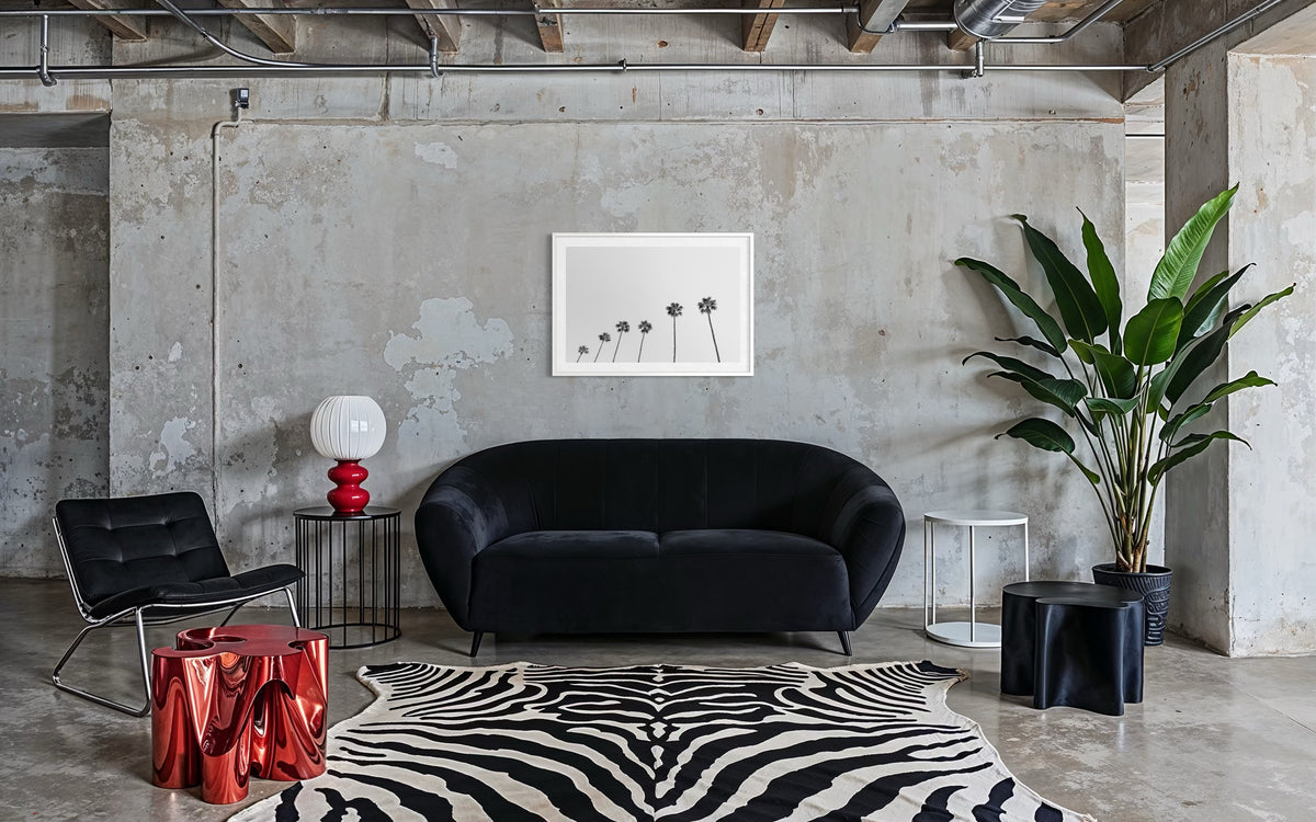 Black sofa with zebra rug, potted palms, and concrete walls in a modern living room setting.