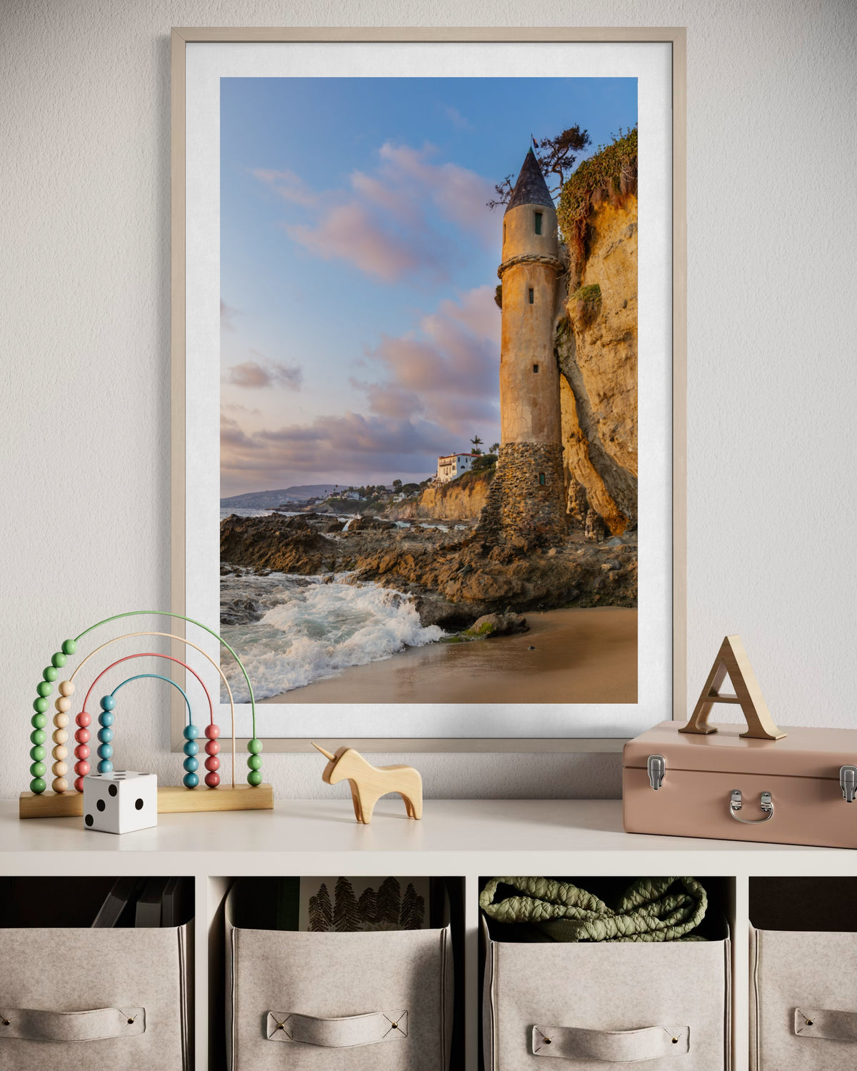 Framed photo of Pirate Tower in Laguna Beach hangs above a child’s shelf with toys and storage baskets.