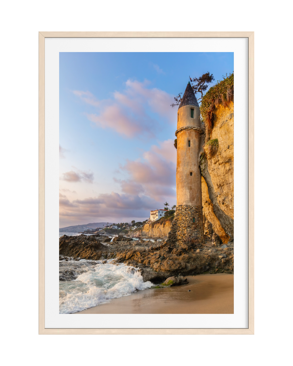 Pirate Tower stands on Laguna Beach at sunset as waves crash below a colorful, cloud-streaked sky.