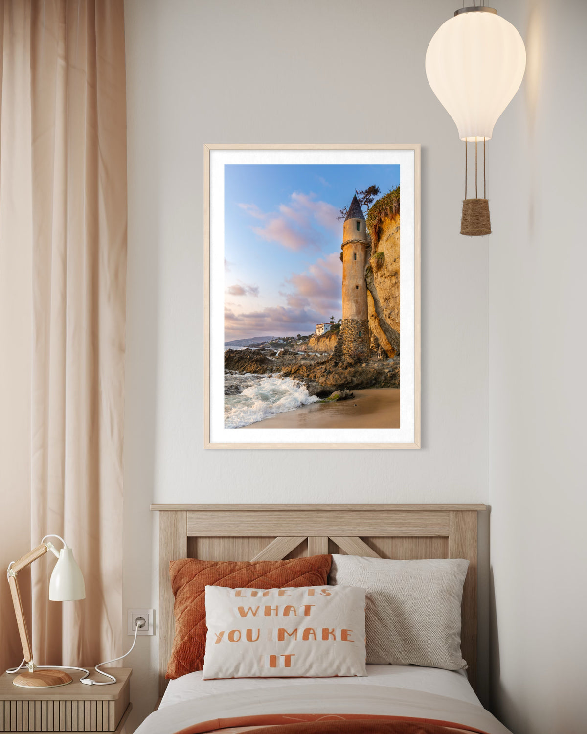 Framed print of Laguna Beach’s Pirate Tower displayed above a bed with an “It Is What You Make It” pillow.