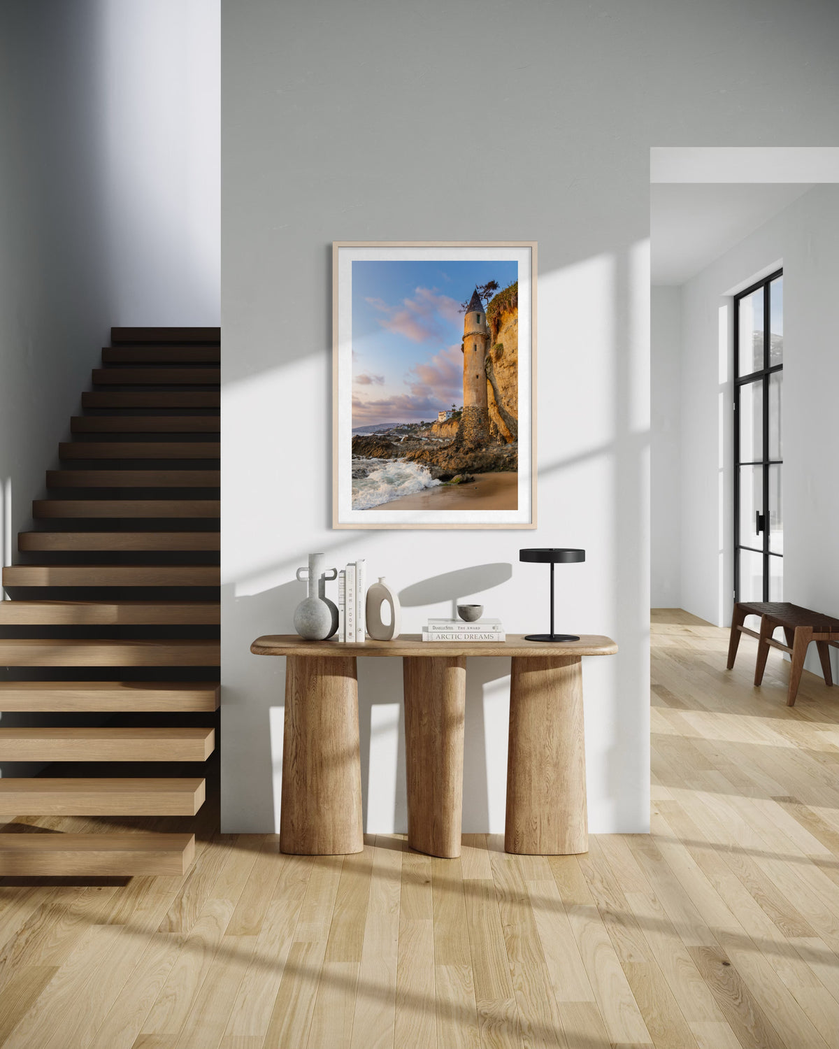 Entryway with wooden console, decor, Pirate Tower photograph from Laguna Beach, and modern staircase in sunlight.