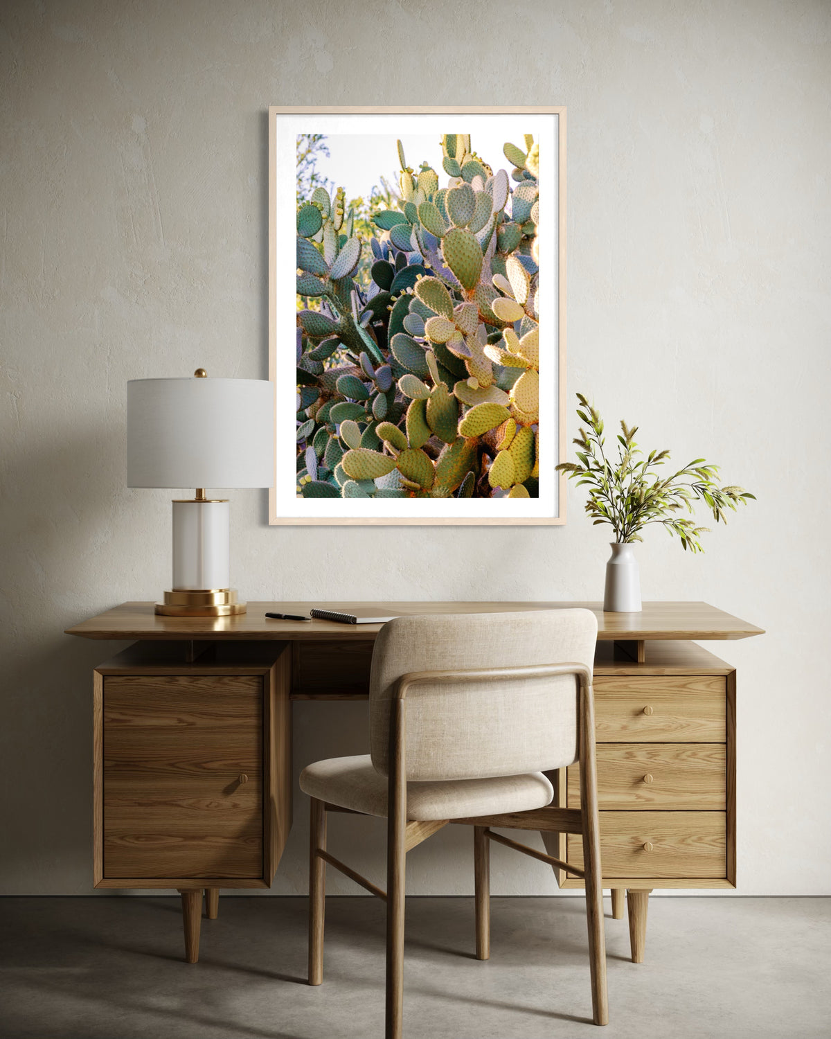 Desk with lamp and plant beneath a framed Prickly Pear cactus print hanging on the wall.