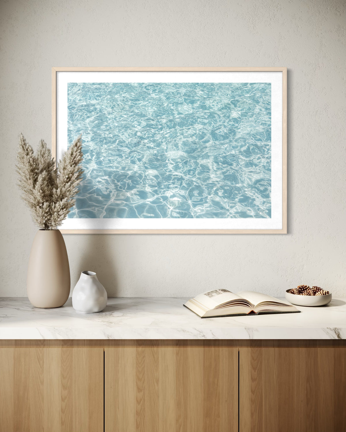 Framed “Refresh II” print above a cabinet with vases, dried grass, open book, and bowl on top.