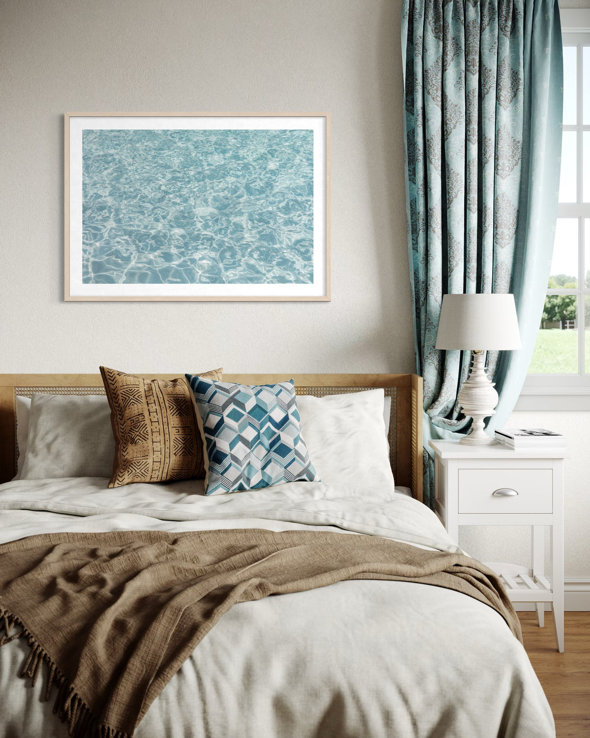 Bedroom with Refresh II bedding, water art above bed, blue curtains, patterned pillows, and white nightstand.