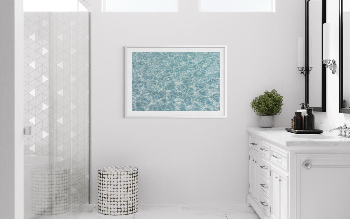 White vanity and round stool in a bright bathroom with glass shower, soft lighting, and water-themed art.