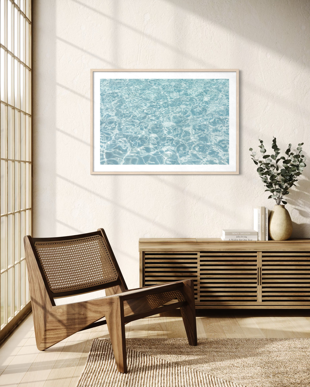 Framed “Refresh II” water photograph hangs above a wooden chair and sideboard in a bright, minimalist room.