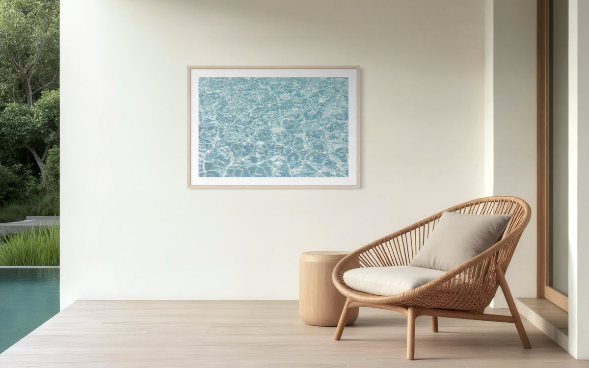 Wicker chair and table next to a pool; “Refresh II” aquatic artwork on a white patio wall.