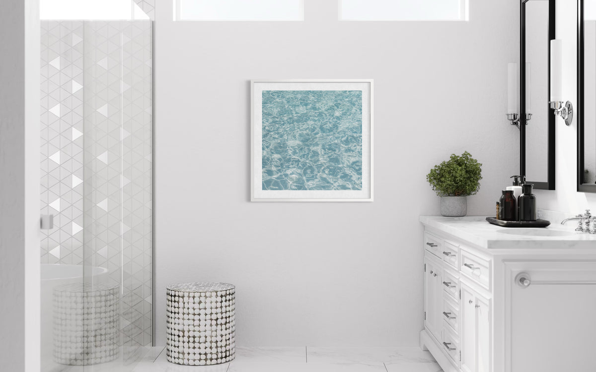Marble bathroom counter, glass shower, and blue artwork create a calm, summery look.