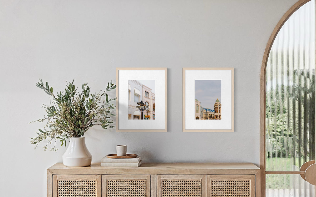 Framed Rodeo Drive photograph hangs on a light gray wall above a wooden console with books and plants.