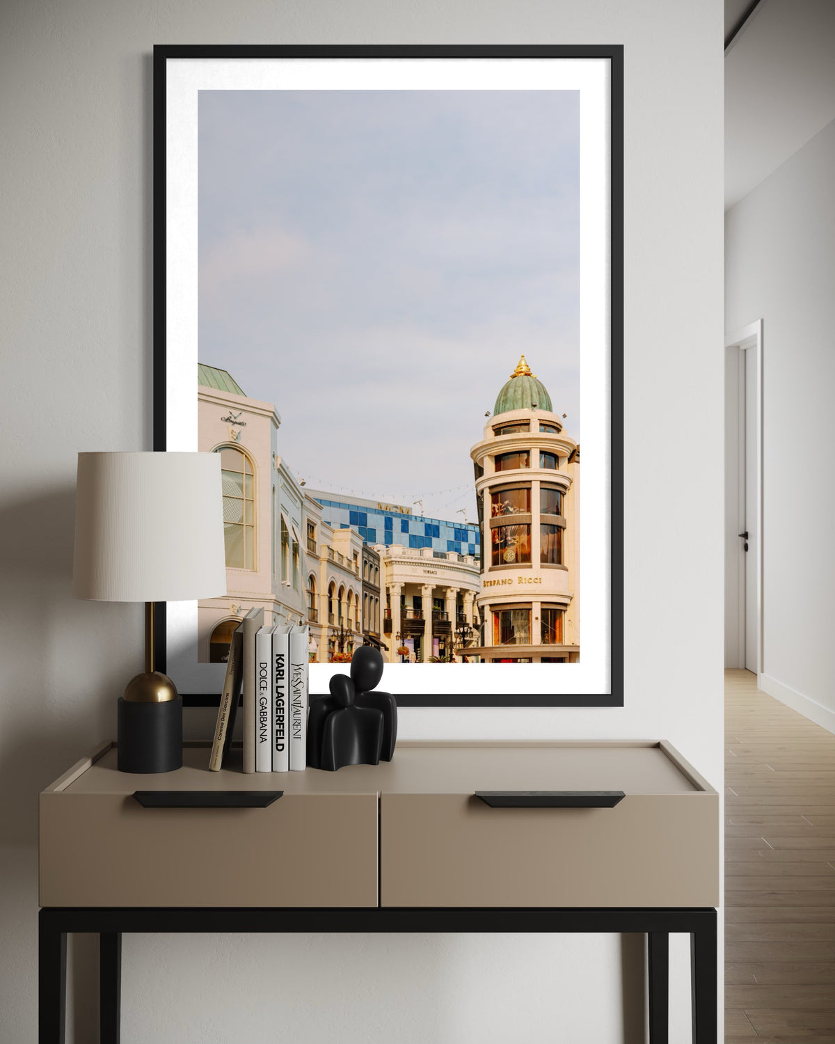 Framed Rodeo Drive street scene photograph, displayed above a beige console table with books and decor.