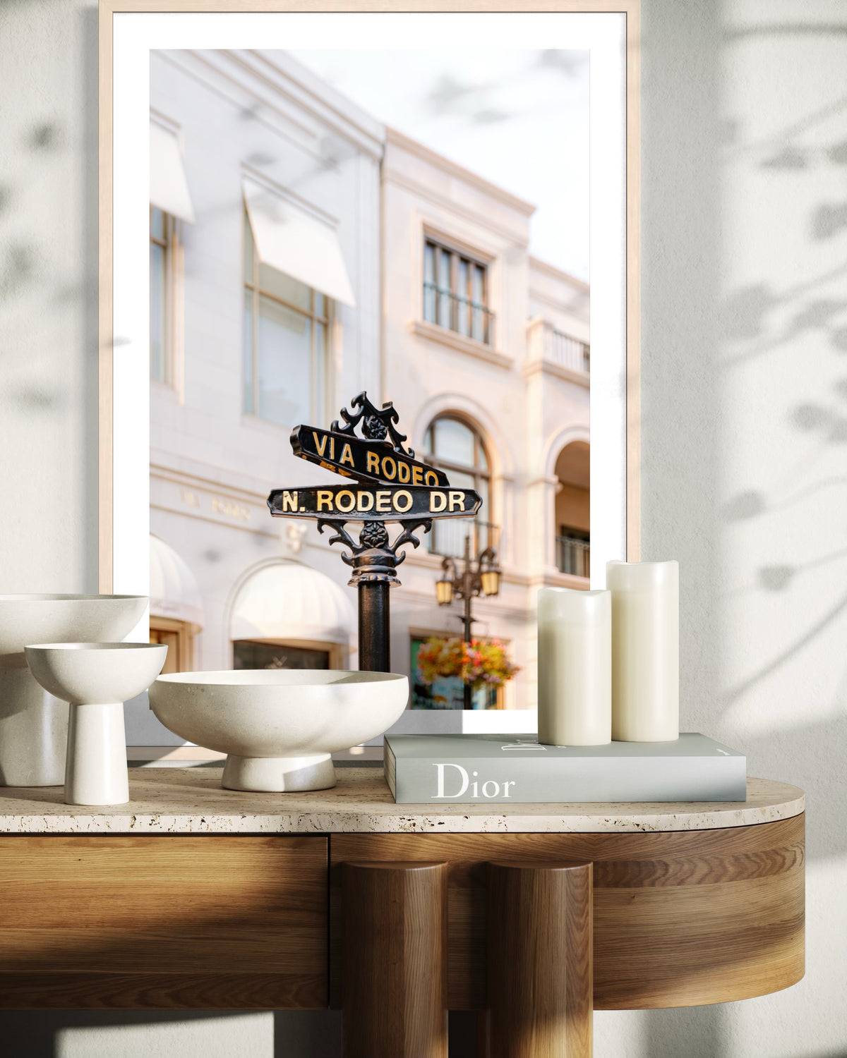 Framed photograph of Rodeo Drive sign from Beverly Hills on a wooden table with candles, bowls, and a Dior book.