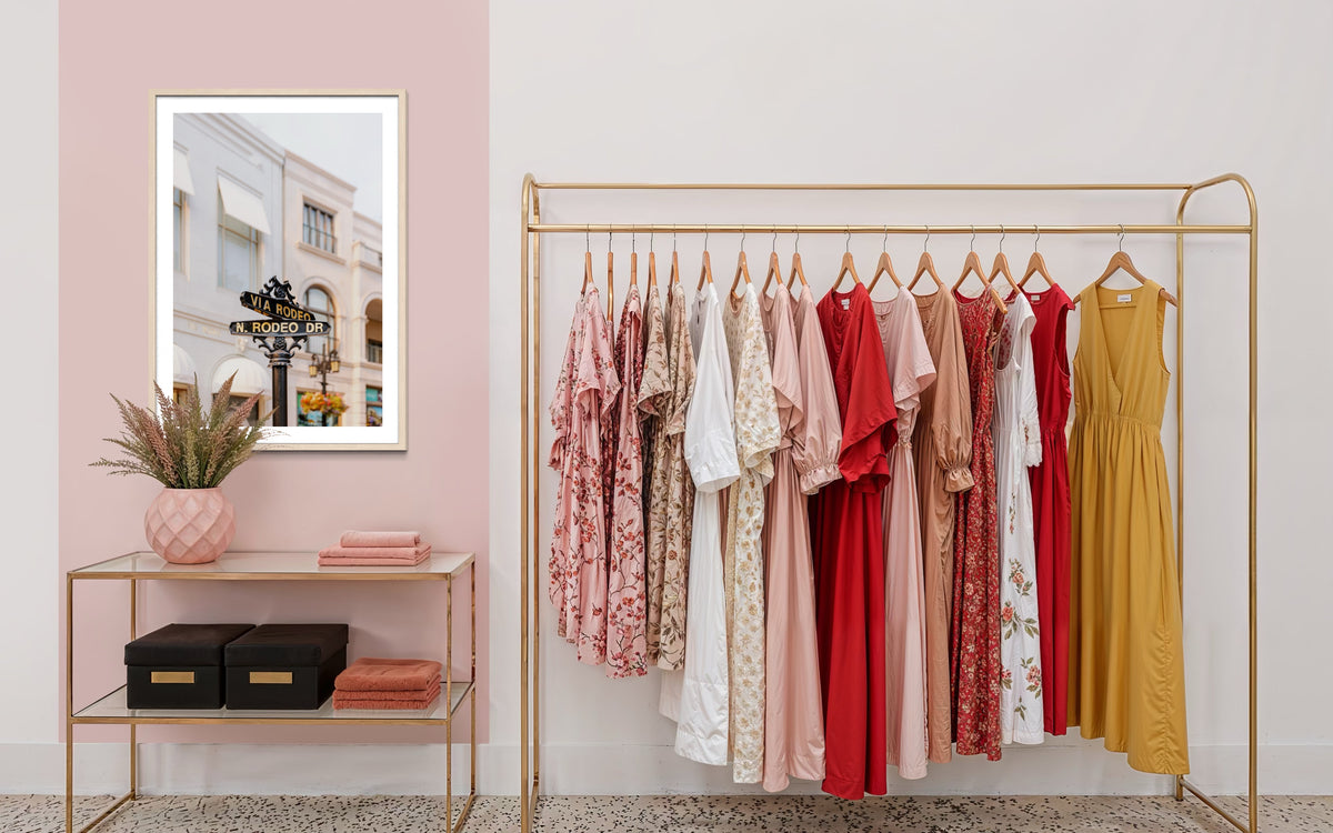 Colorful dresses hang on a rack beside luxury decor and a Rodeo Drive sign in Beverly Hills.