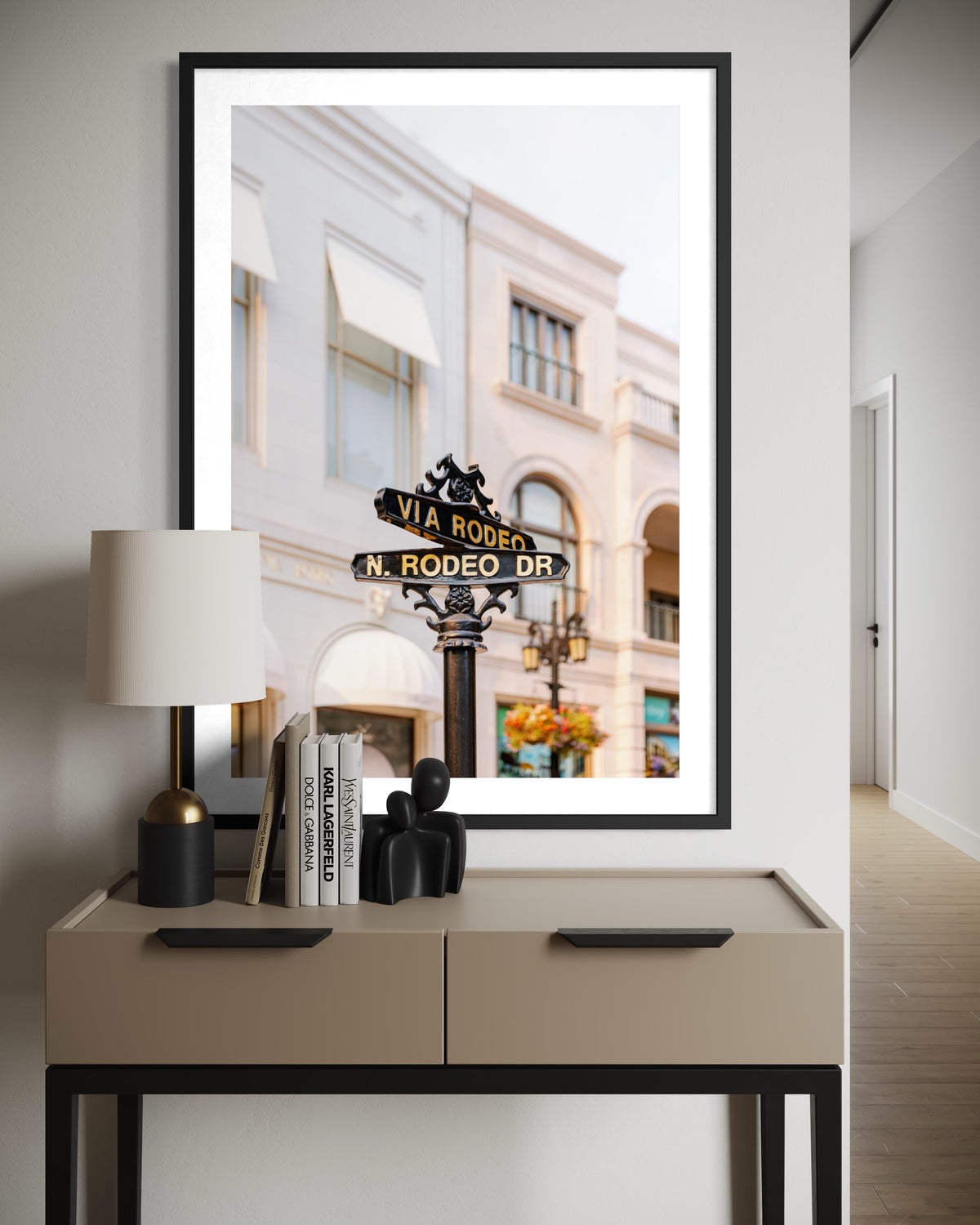 Framed photo of the Rodeo Drive street sign in Beverly Hills, hung above a table with decor and books.