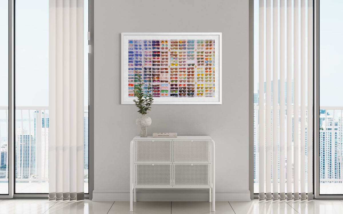 White cabinet, vase, and Shades of Summer art print hang on a gray wall between tall windows in a modern room.