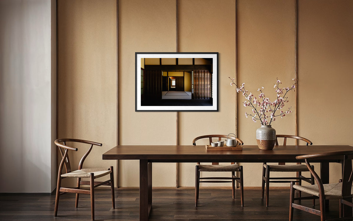 Minimalist dining area in Shōya House, four wood chairs, pink flowers, wall art, warm lighting.