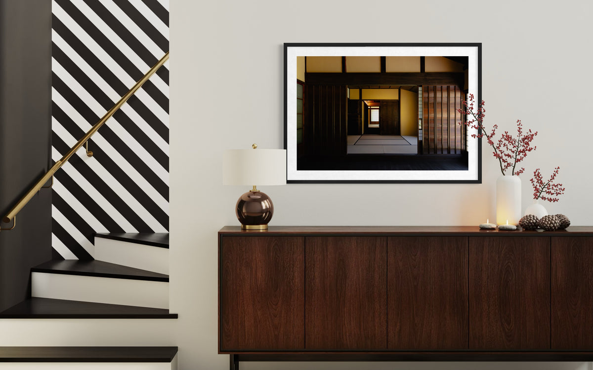 Modern entryway in Shōya House, Japan, with striped stairs, wood sideboard, framed art, lamp, and decorative branches.