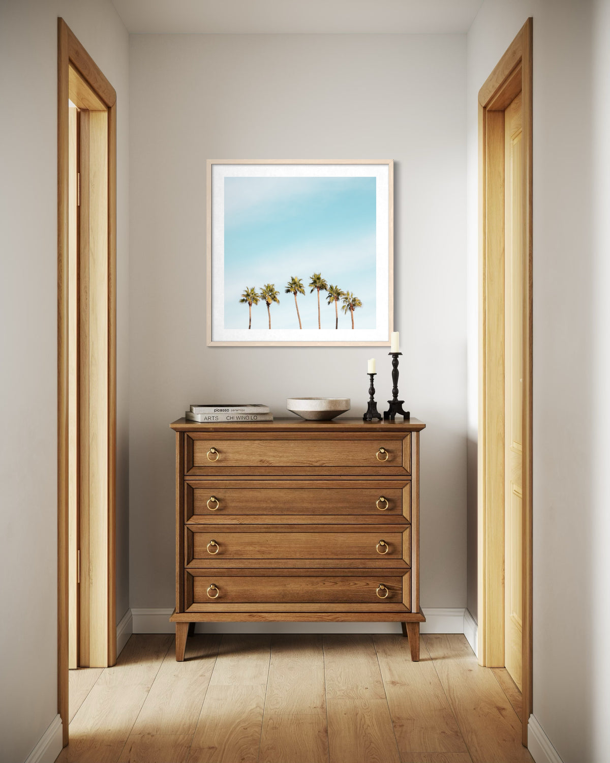 Dresser with books, candles, and palm print art in a bright hallway, photographed in Palm Springs.