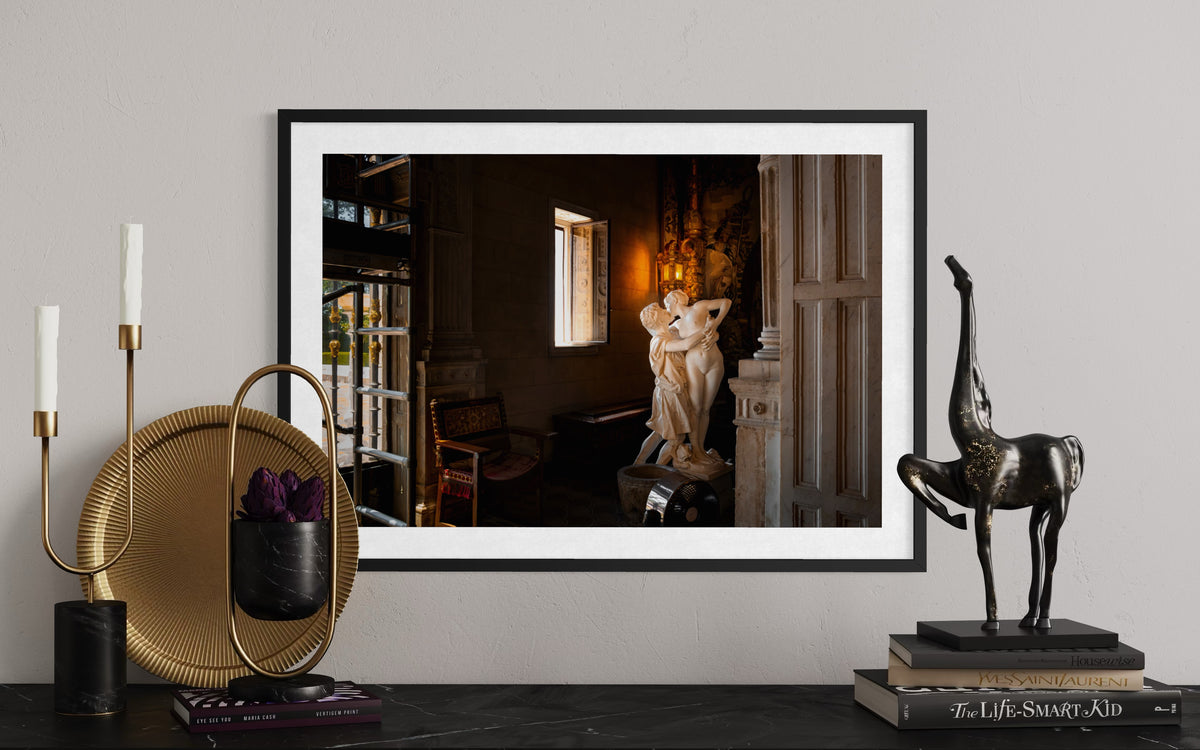 Framed “Stolen Kiss” photograph with warm lighting beside a giraffe sculpture on a modern console table.