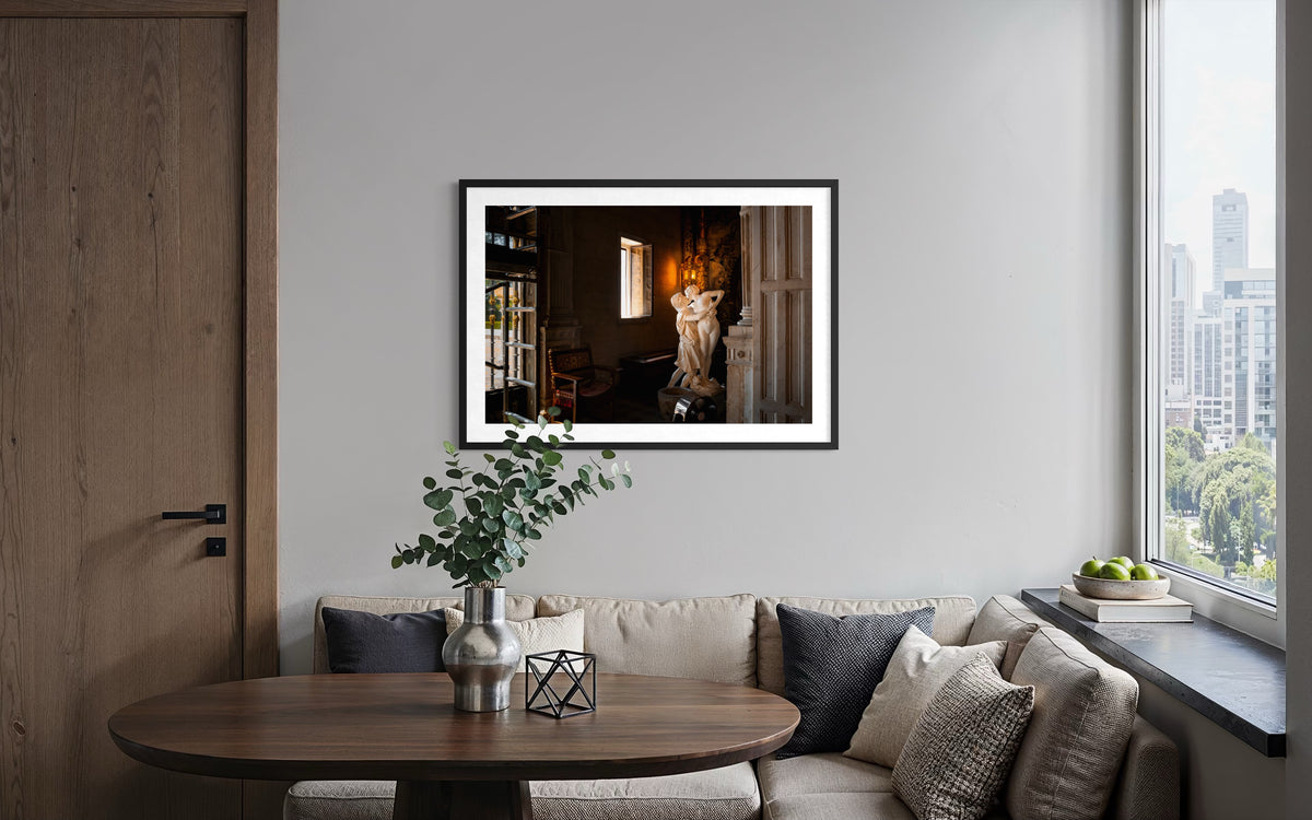 Framed “Stolen Kiss” photo above a beige sofa, warmly lit modern living room with large windows.