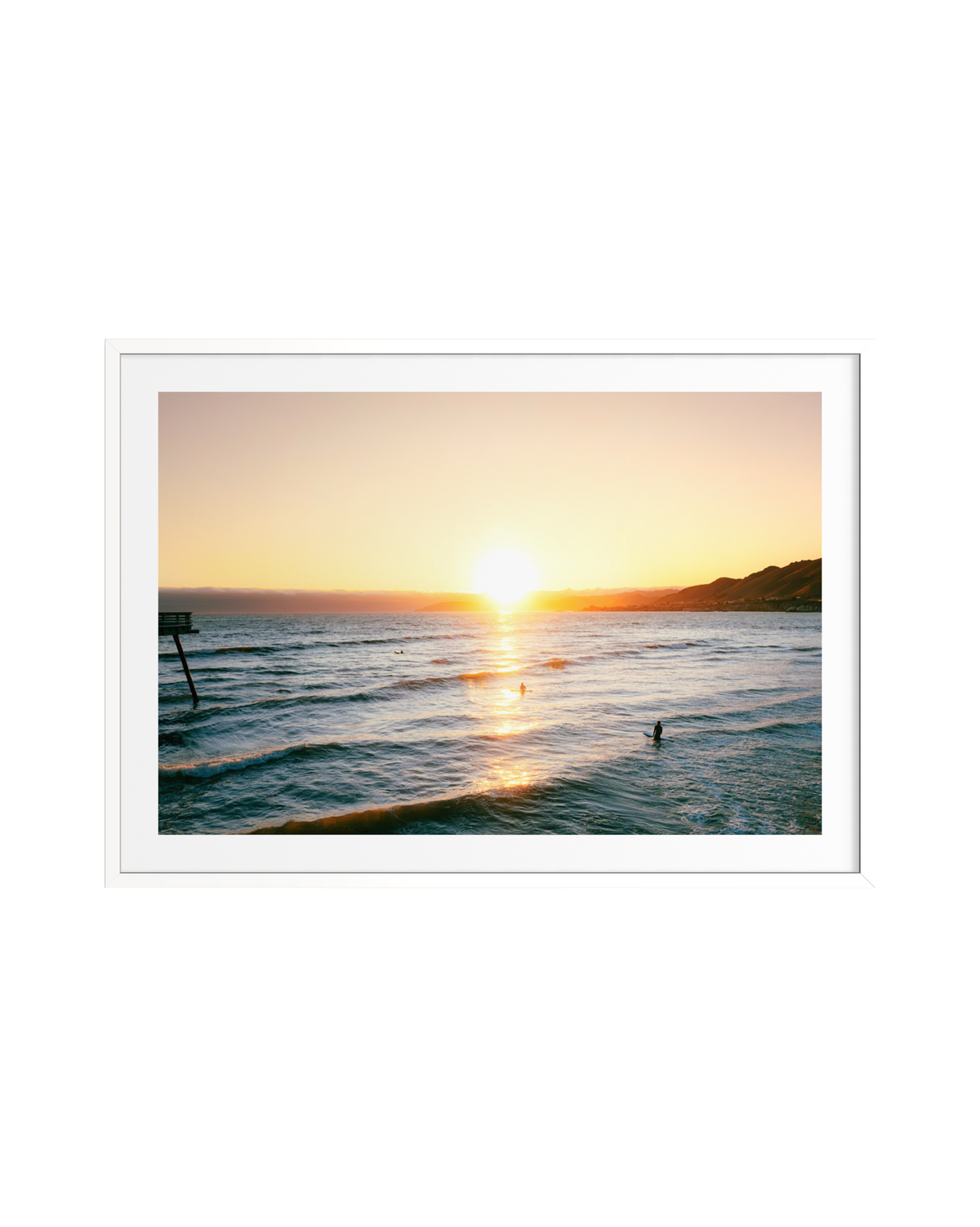 Surfers ride gentle evening waves at Pismo Beach as the sun sets and a few people enjoy the shore.