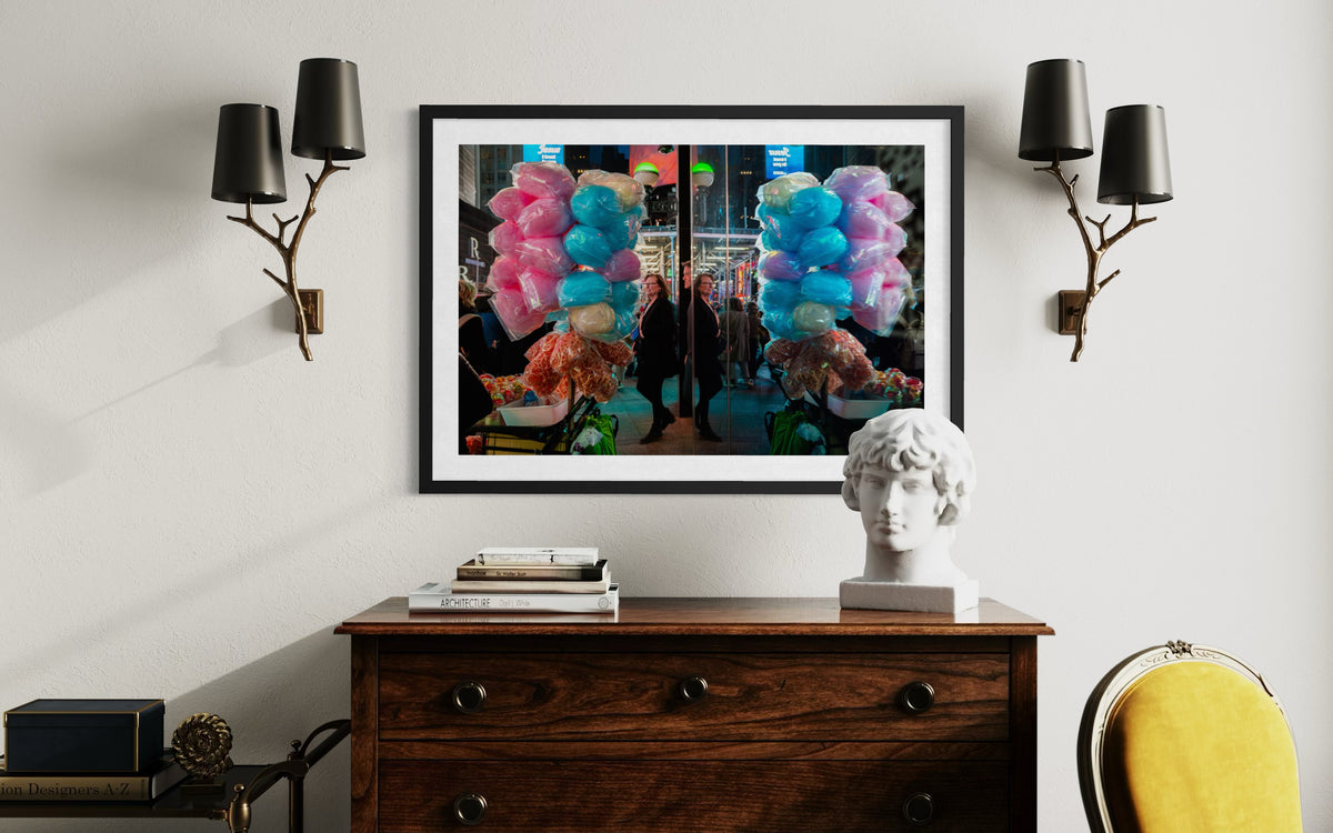 Cotton candy sellers on a street, photo displayed above a dresser with books, bust sculpture, and black sconces.
