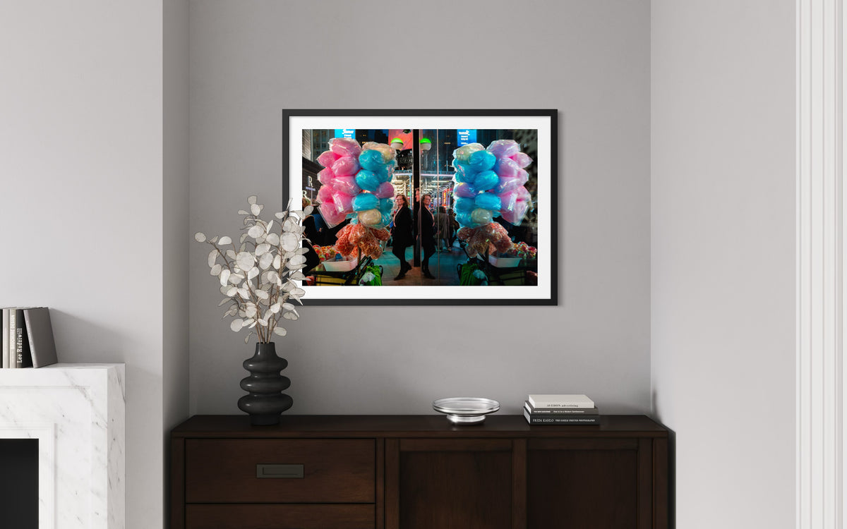 Framed photo of a cotton candy street stand in NYC above a dark wood console with a vase and small decor items.