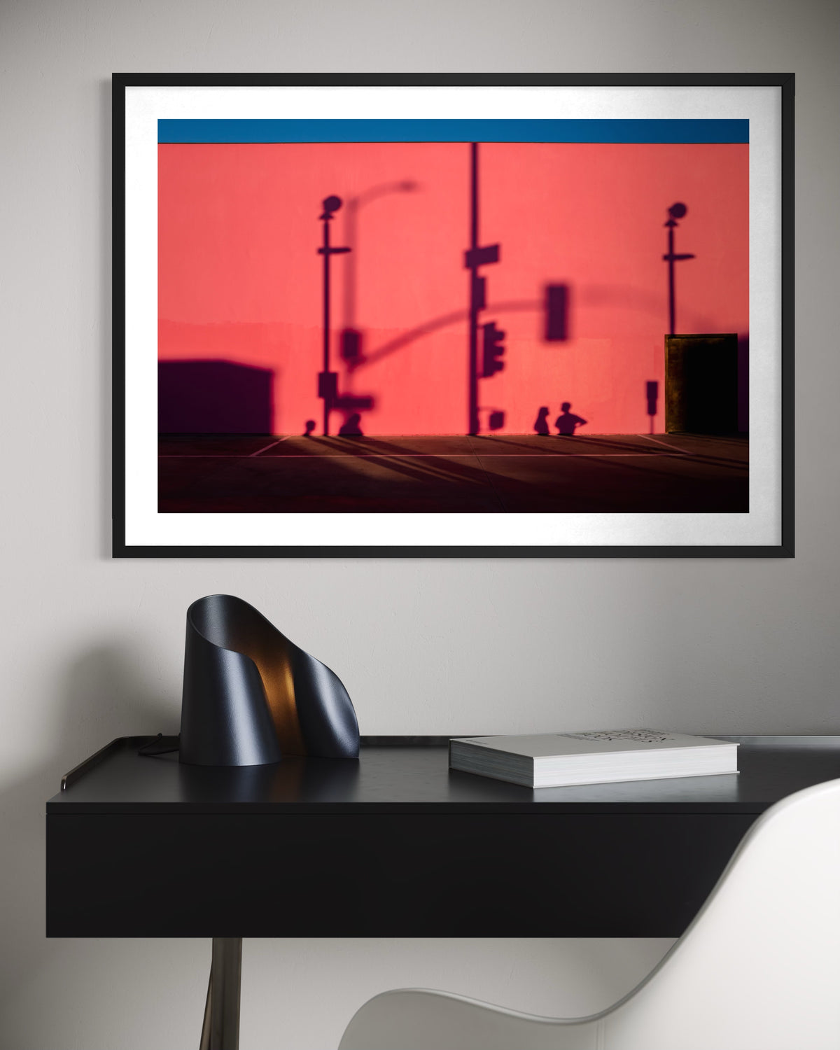 Framed print of ‘That Pink Wall’ Los Angeles photo displayed above a black desk with chair and books.