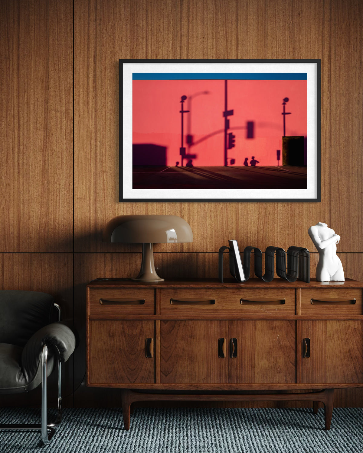 Wood-paneled room with sideboard, lamp, books, and a framed “That Pink Wall” Los Angeles photo among decor.