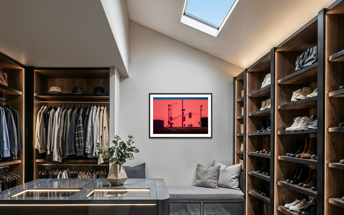 Shelves and hanging clothes line a modern walk-in closet, with That Pink Wall Los Angeles photo art by a skylight.