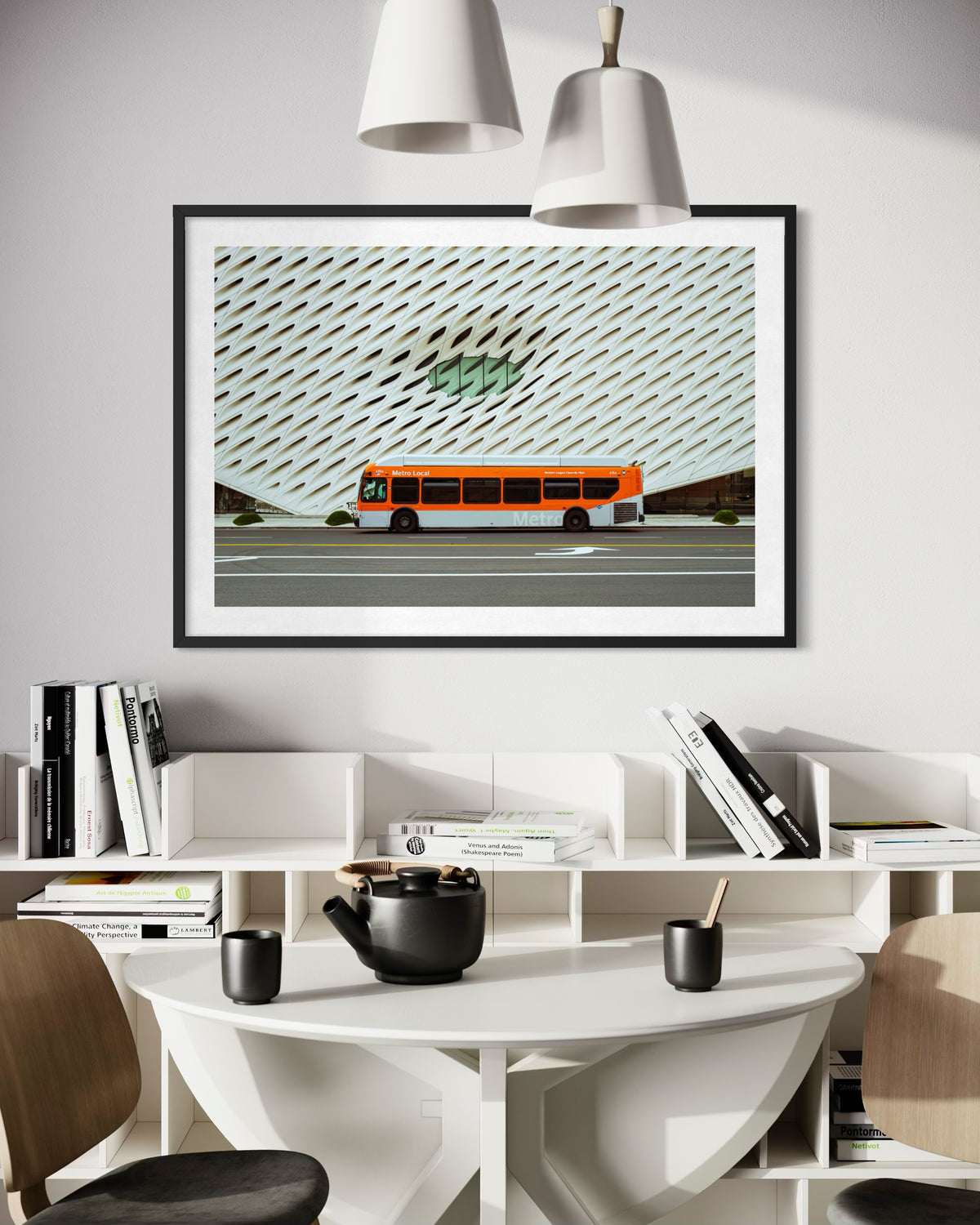 Framed photo of a Metro bus at The Broad, Los Angeles, displayed above a white table with books and a teapot.