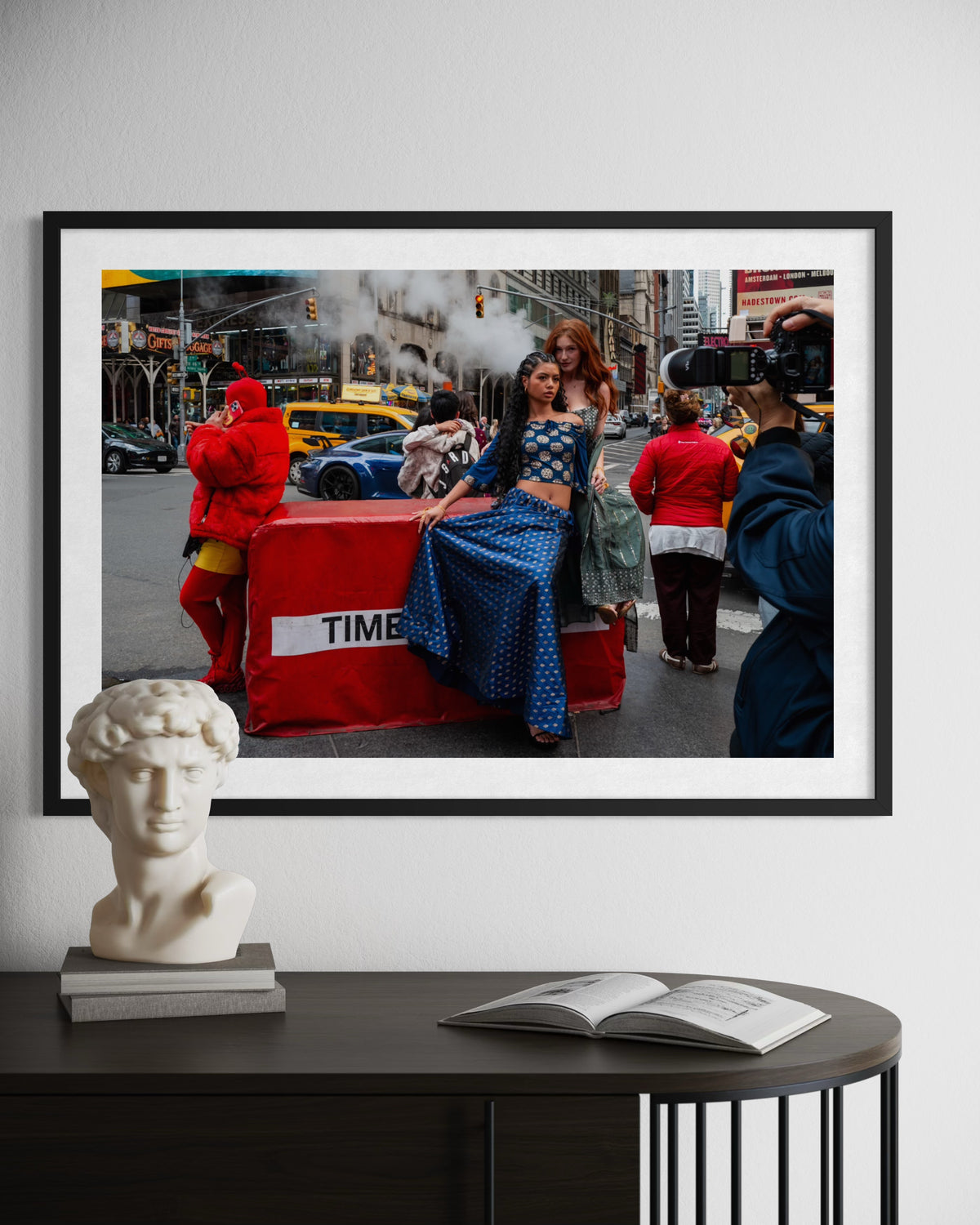 Framed NYC photo of women, taxis, and steam in Times Square; bust sculpture and book underneath.