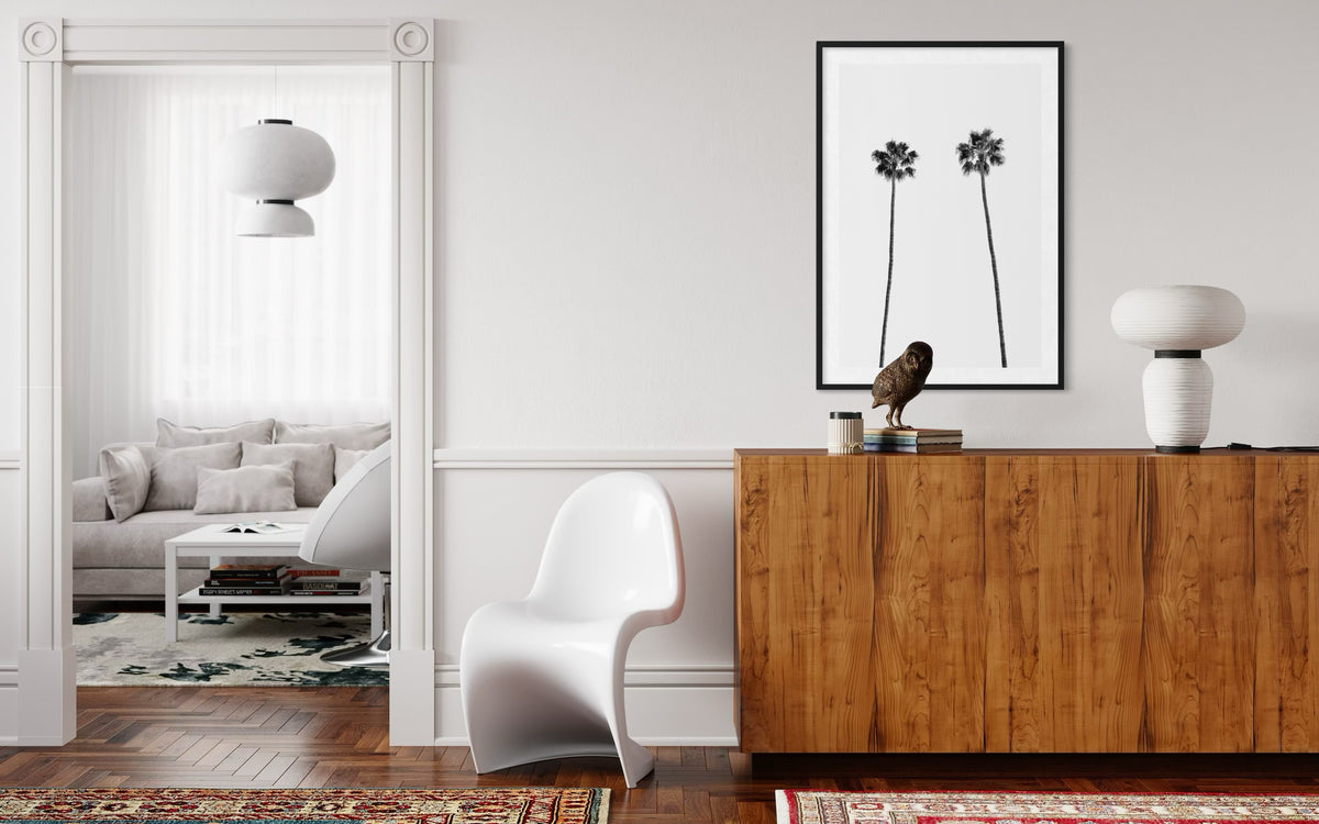 White chair and wood cabinet in a living room with Twin Palms art and minimal wall decor.