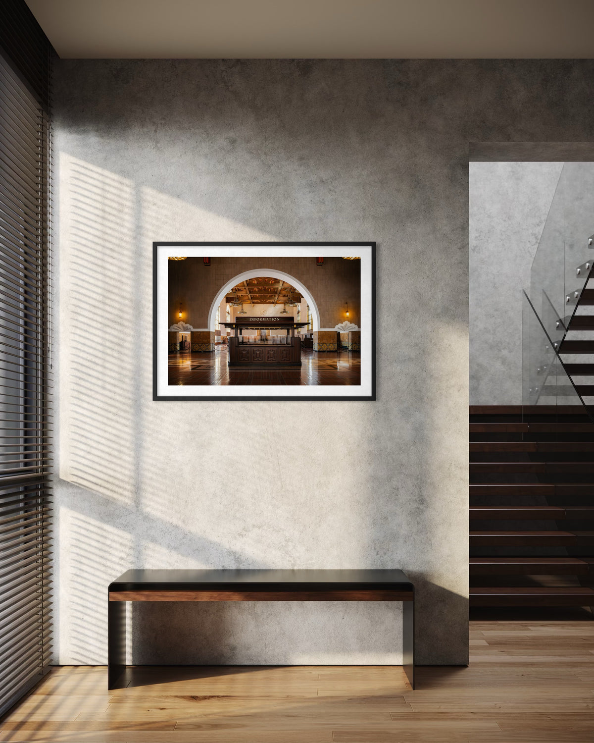 Framed Union Station Information sign hangs above a bench near stairs in a sunlit room, gray wall background.