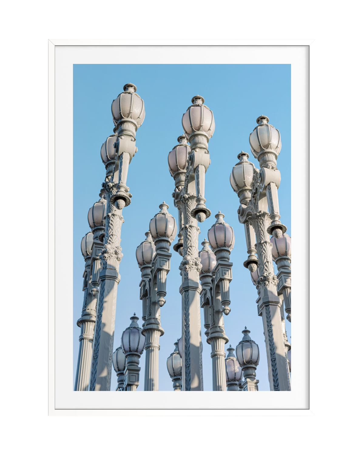Vintage Los Angeles street lamps from Urban Light stand under a blue sky with a white border.