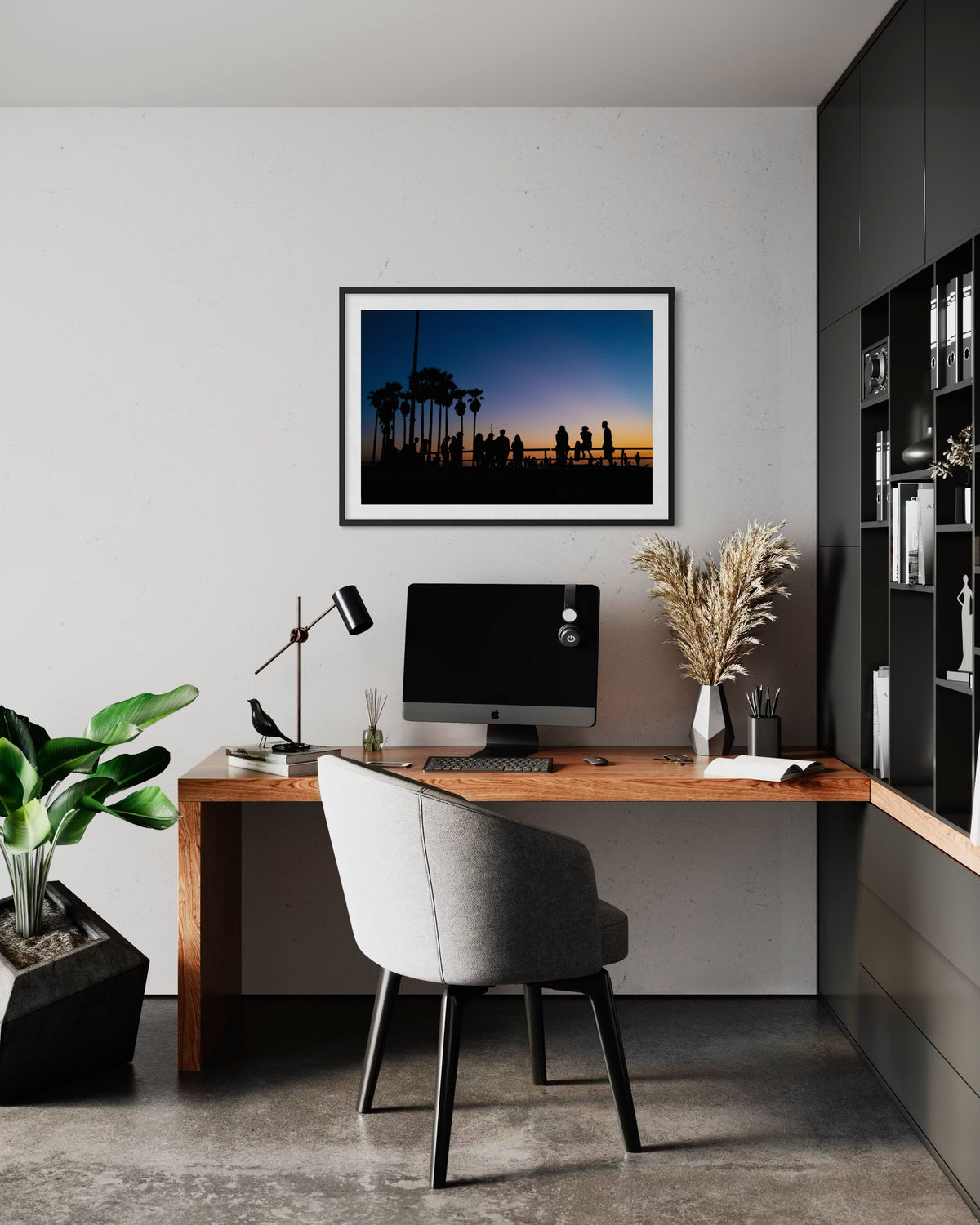 Framed “Venice Beach Summer Night” print on wall above wooden desk, computer, gray chair, and plants.