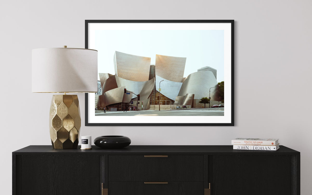Gold lamp and black console beneath a Walt Disney Concert Hall photo on a white wall, Los Angeles.