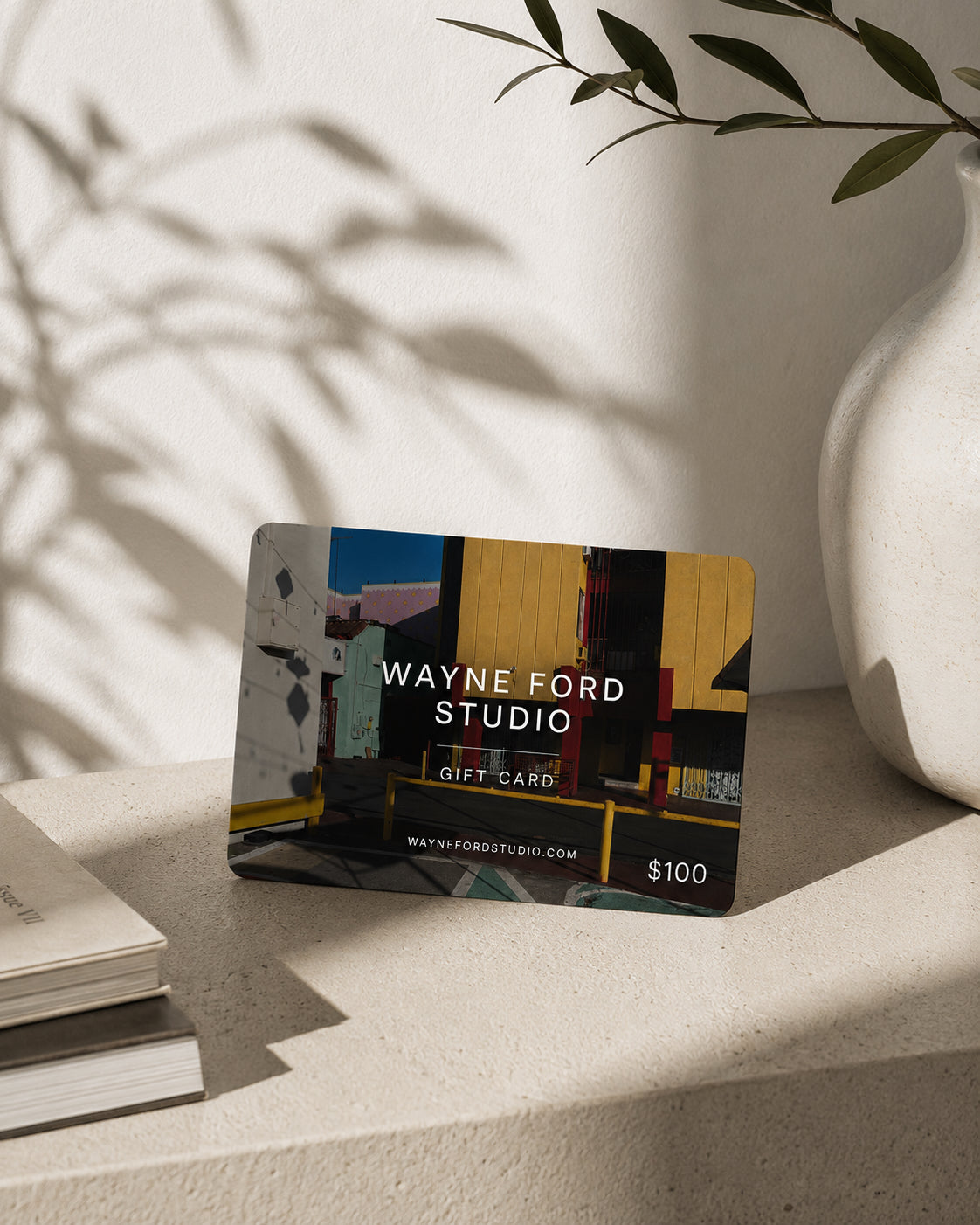 Wayne Ford Studio Gift Card on a beige surface next to a plant and stacked books.