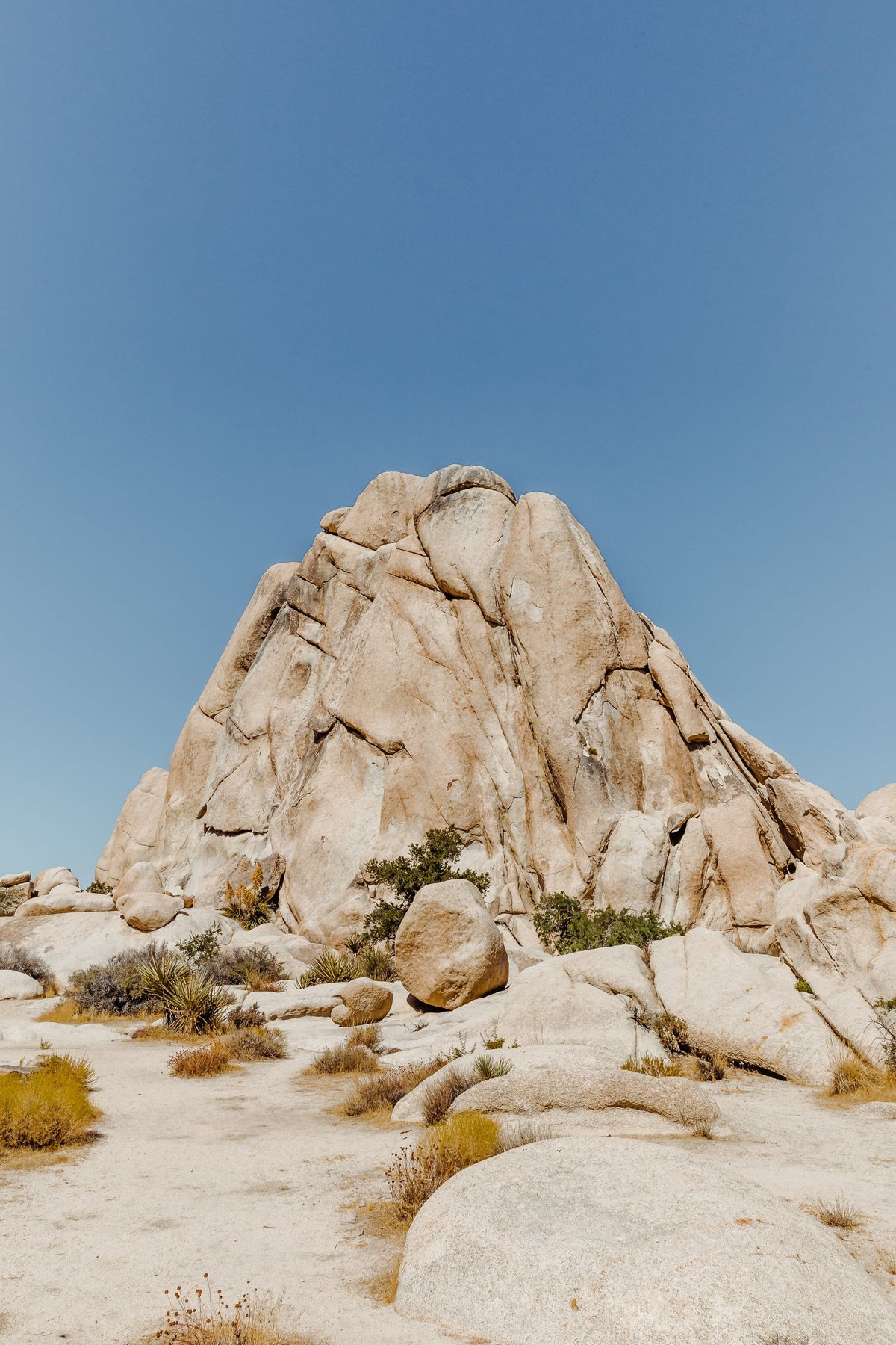 Large rock formation rises among sparse desert plants under a clear blue sky.