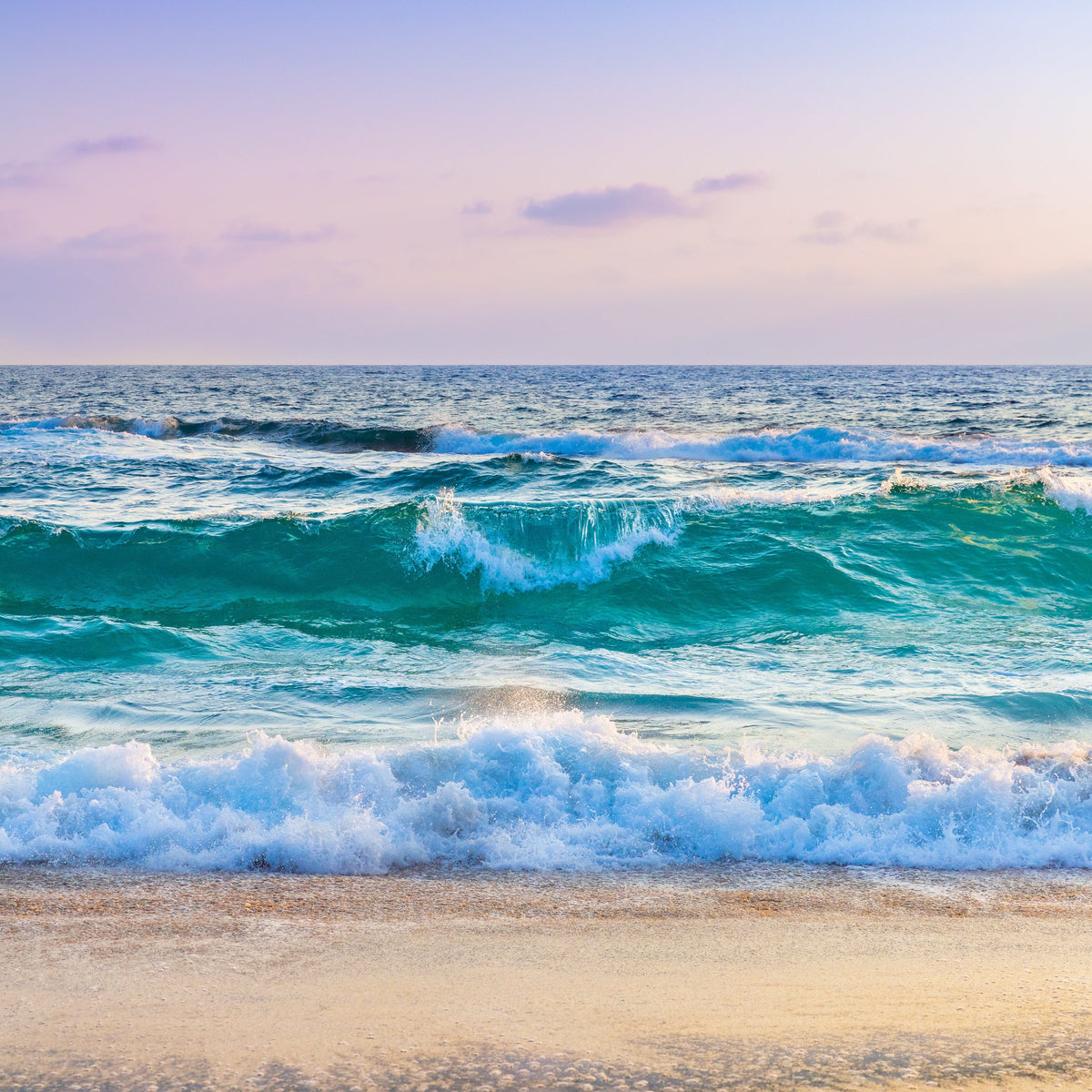 Sunset waves roll onto sandy Pacific beach under a pastel sky.