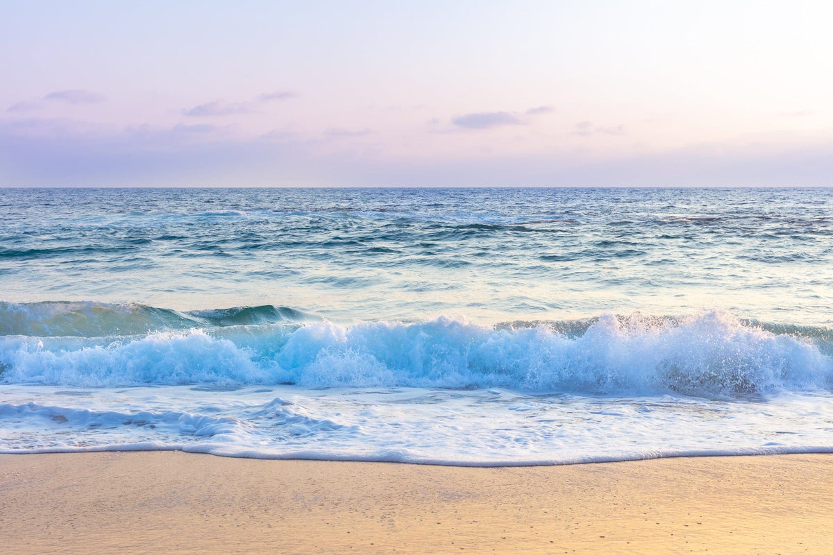 Gentle waves wash onto Laguna Beach’s sandy shore beneath a soft, pastel sunset sky.